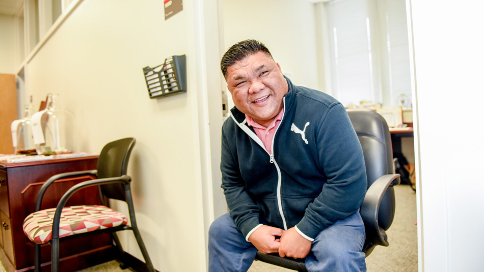 FBNS' Fred Jimenez sits in the door of his office, smiling as he leans forward to check on a coworker down the hall.
