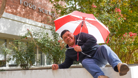 FBNS' Fred Jimenez laughs while holding an umbrella in front of Schaub Hall.