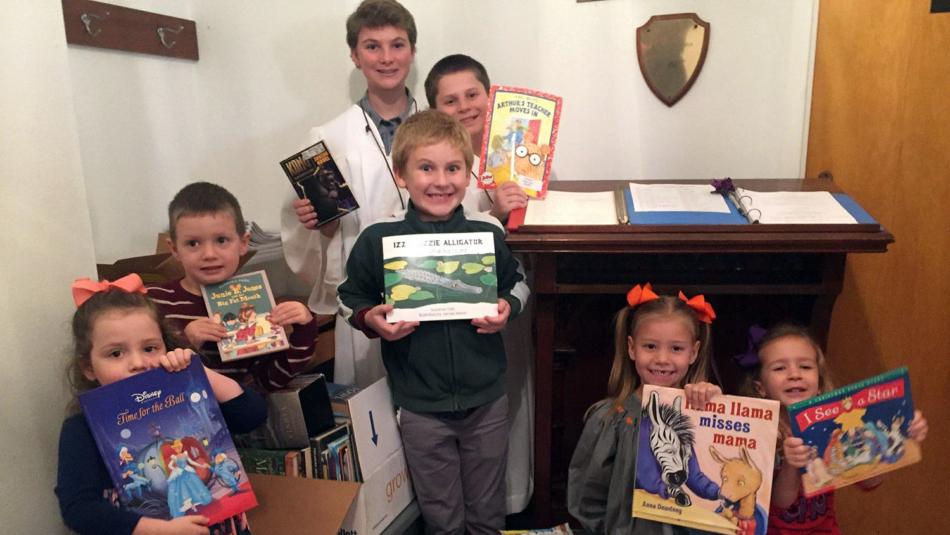 A group of students standing with a 4-H student holding up the books they collected for Hurricane Florence victims