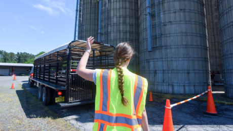 A woman with a long braid and a reflective vest motions for a big trailer to back up.