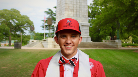 CALS student Collin Blalock stands in front of the NC State Bell Tower in a baseball cap advertising his produce business.