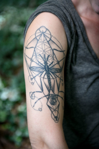 A close-up photo of an artistic tattoo of a mosquito surrounded by geometrical elements on a woman's humerus.
